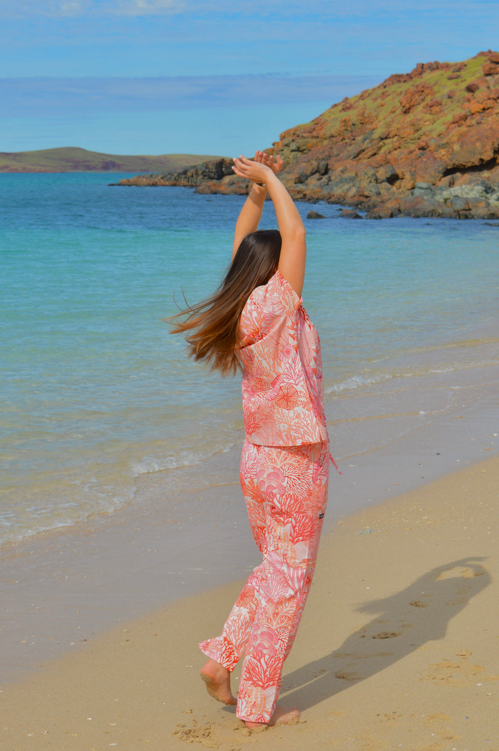 Person in a pink floral outfit standing on a beach with ocean and rocks in the background