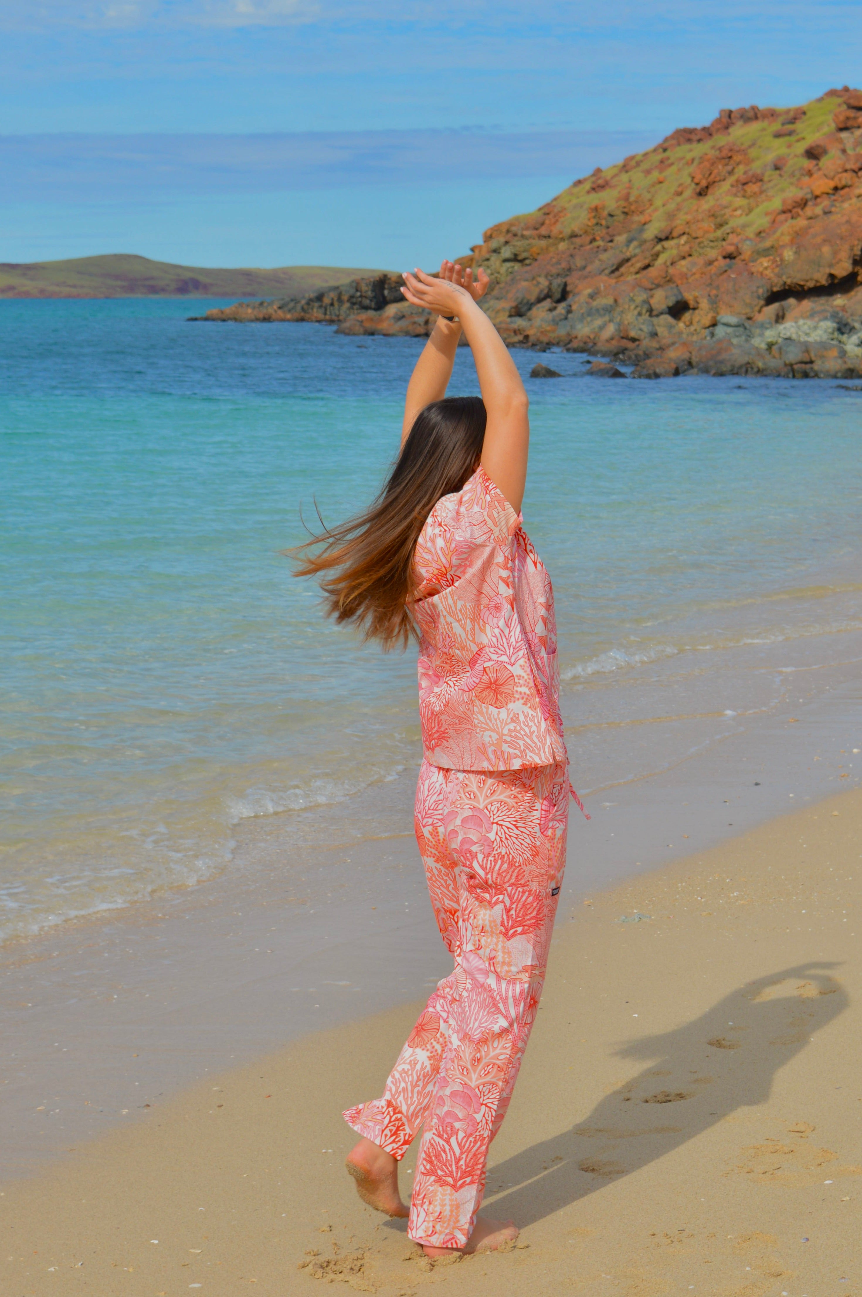 Person in a pink floral outfit standing on a beach with ocean and rocks in the background